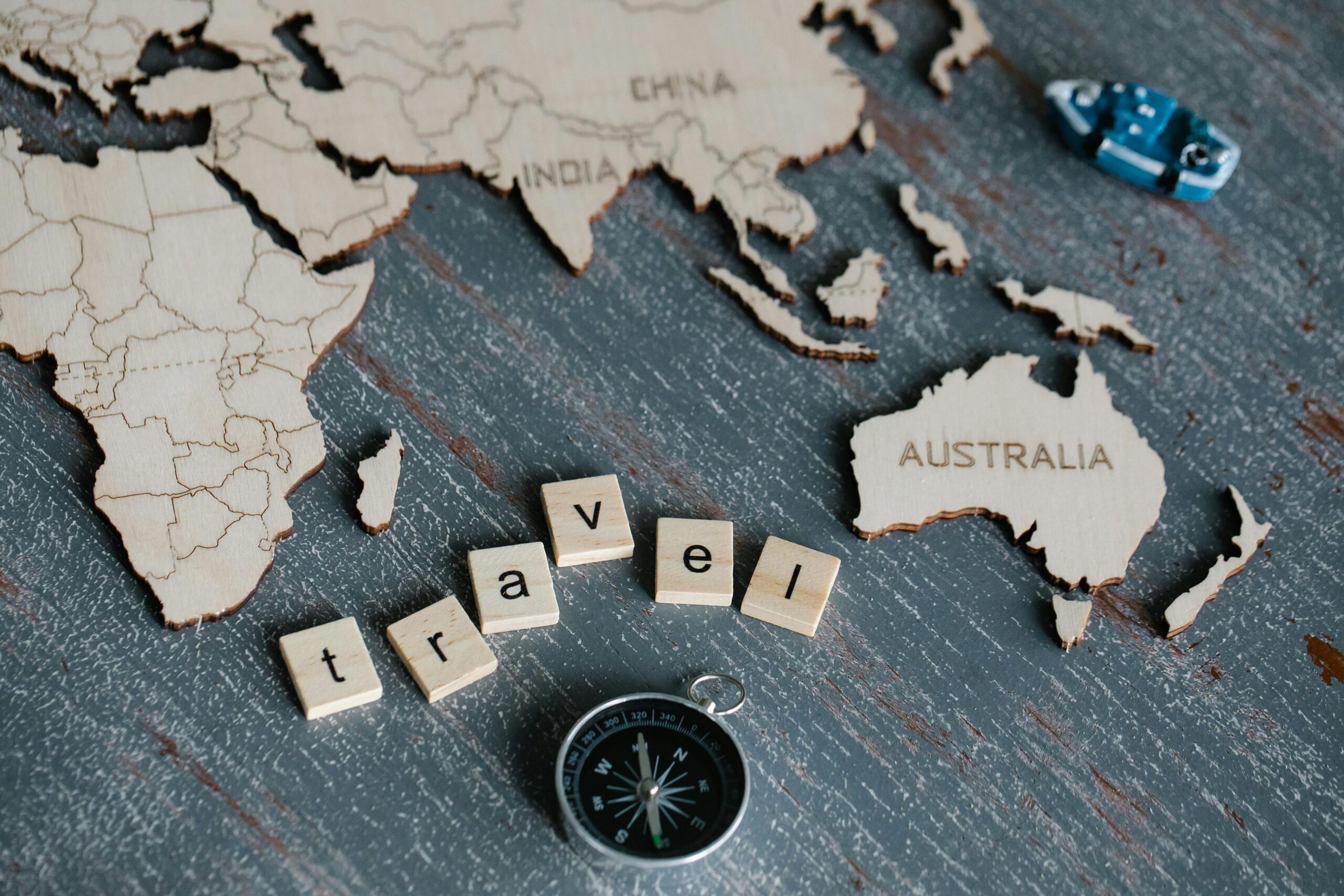 Creative travel concept featuring a wooden world map, compass, and scrabble letters spelling 